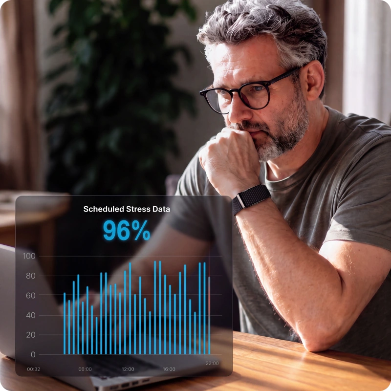 A man working at a laptop wearing the HLTH Band, with his stress data charted beside him