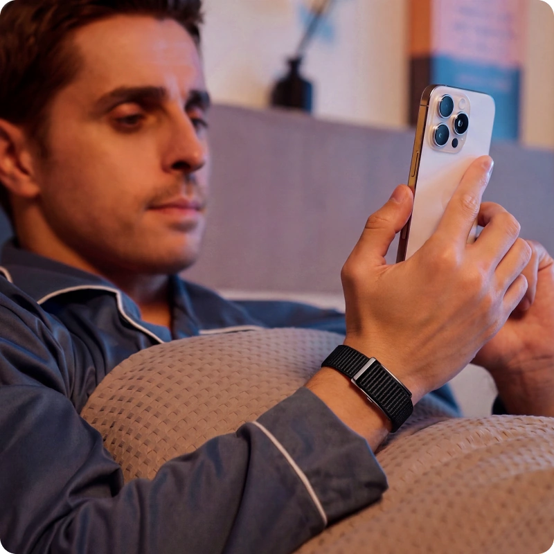 A man relaxing on a sofa checking his HLTH Band data on his phone