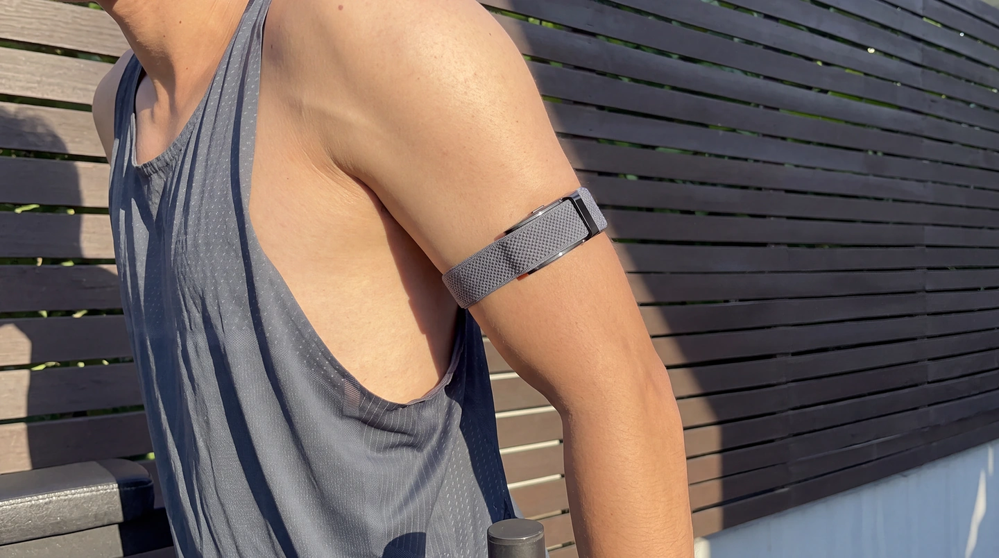 A runner outdoors in a training vest, the HLTH Band worn on the upper arm in a grey knit arm band