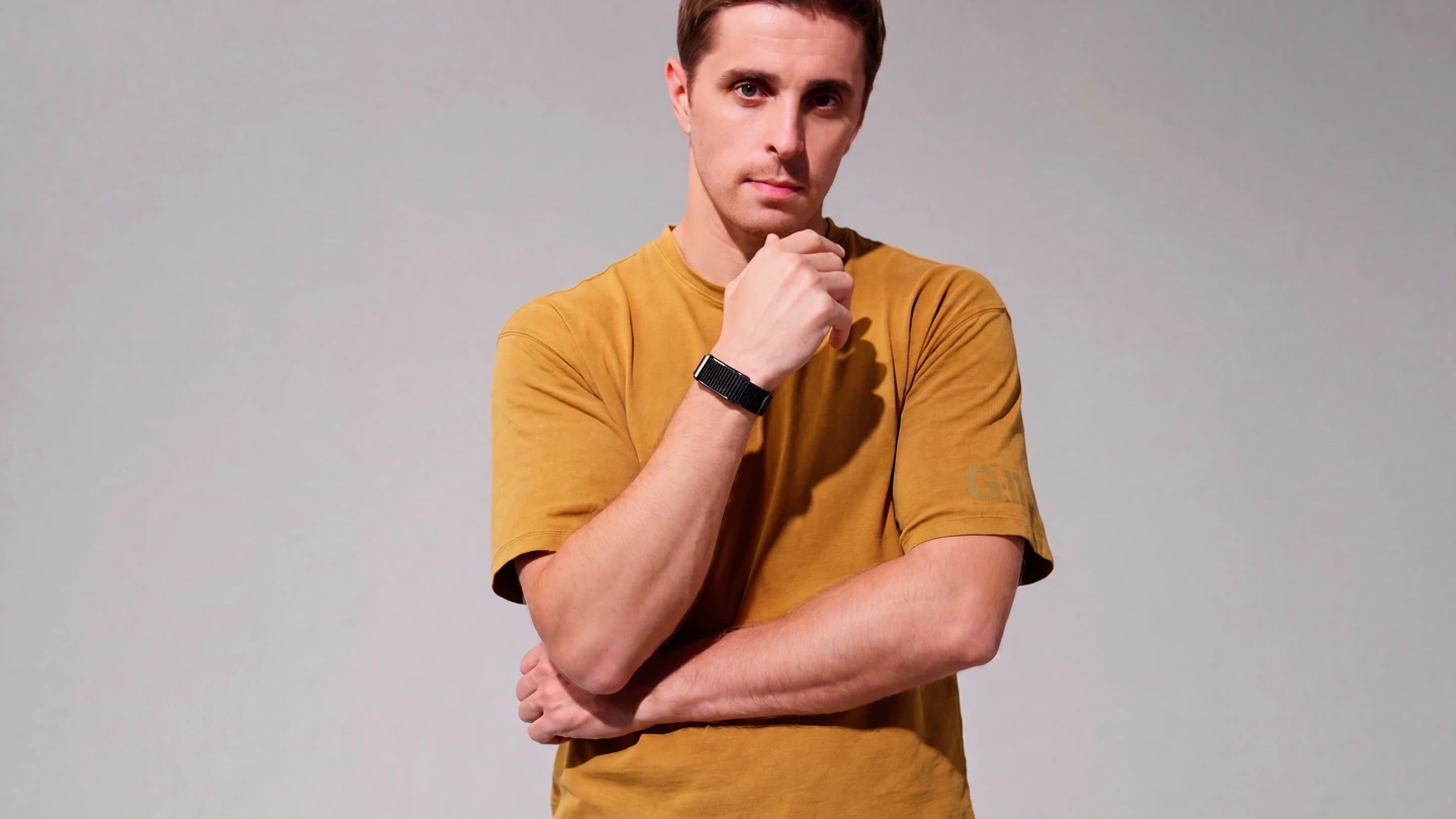 A man against a plain grey background with one hand raised to show the HLTH Band on his wrist