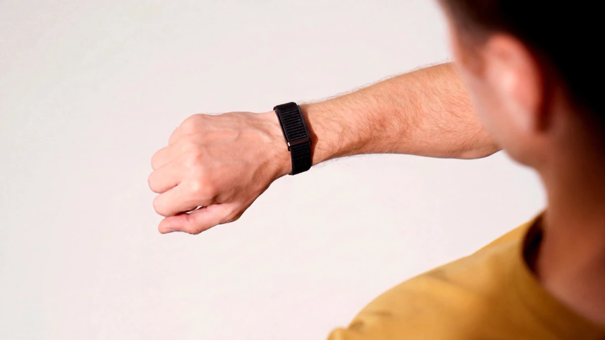 A man's forearm held out against a plain wall, the HLTH Band on the wrist