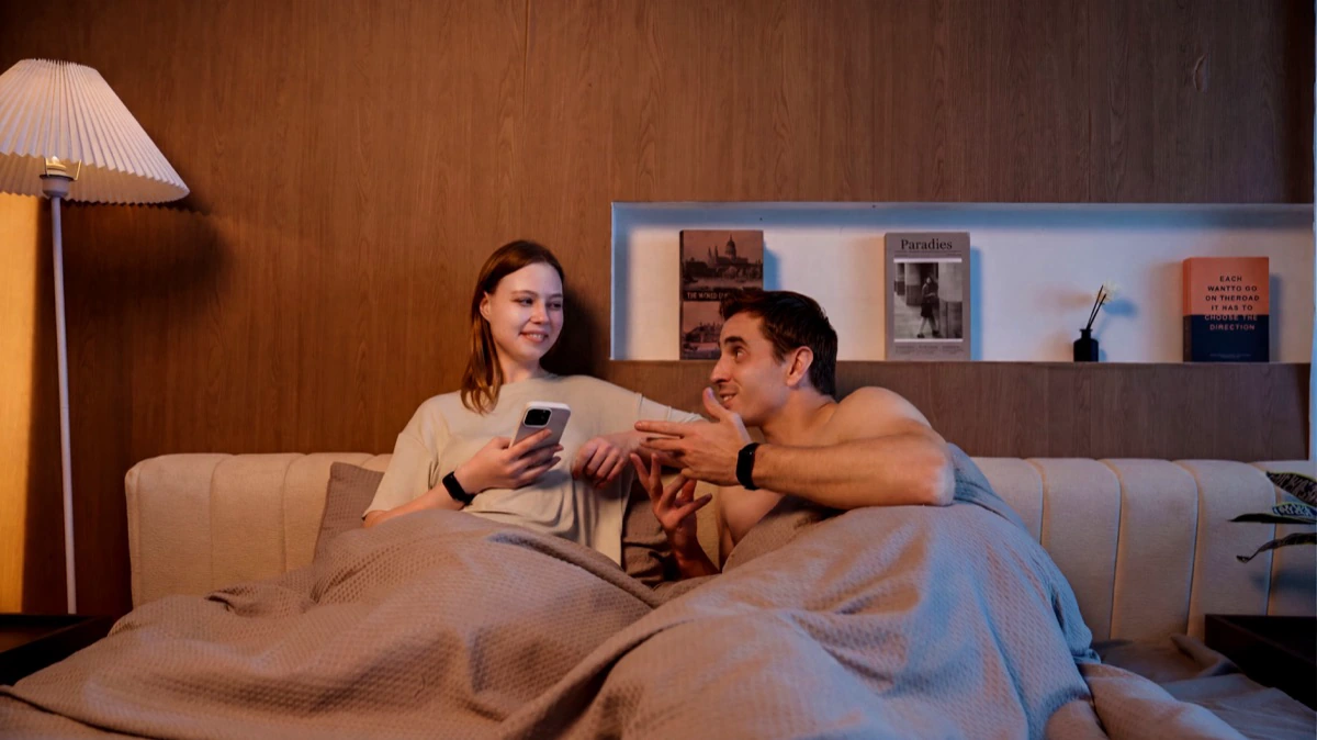 A couple sitting up in bed at night talking, both wearing the HLTH Band