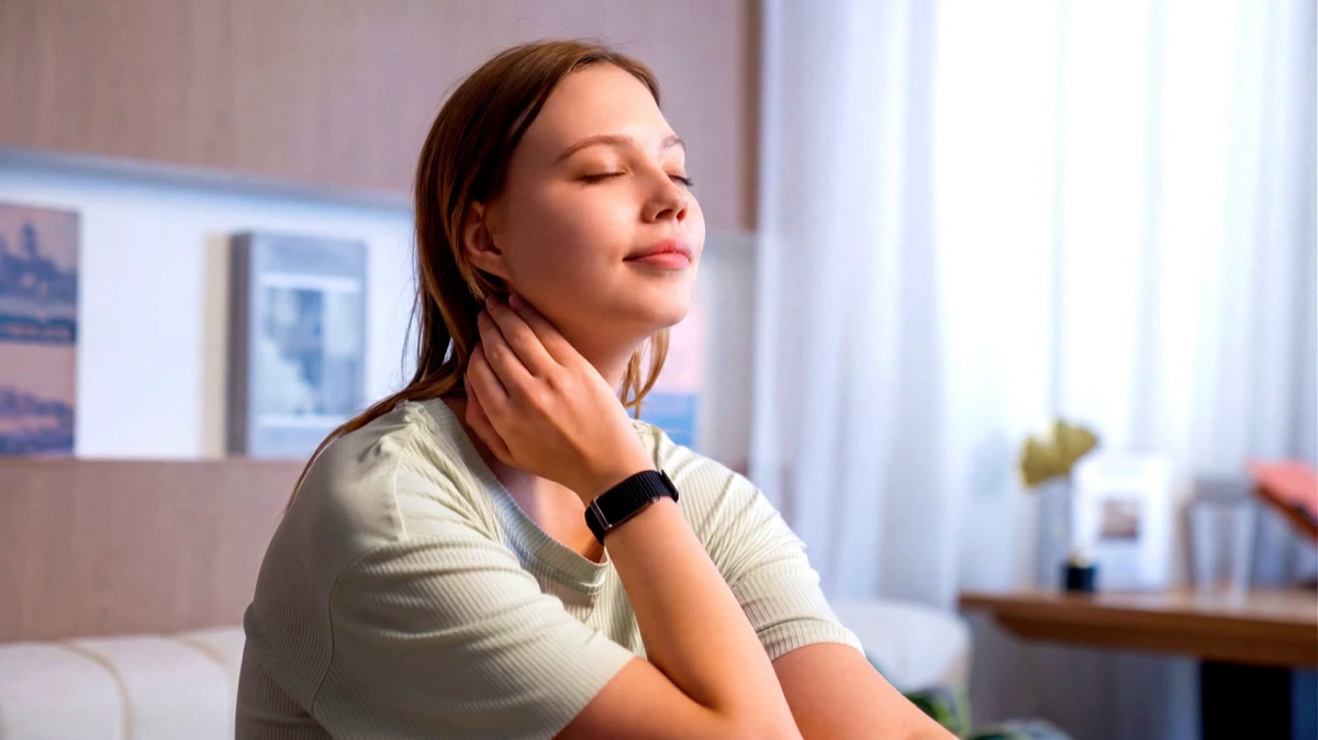 A woman sitting on a sofa with her eyes closed, two fingers held to her neck, the HLTH Band on her wrist
