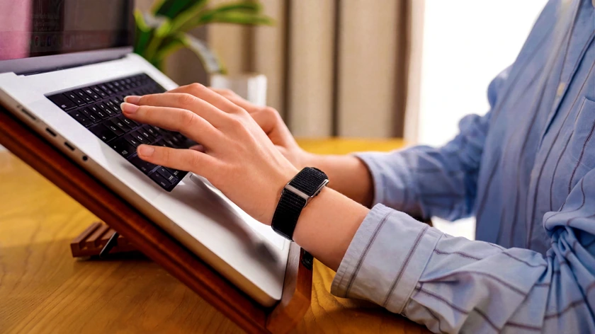 Someone working at a laptop, wearing the HLTH Band
